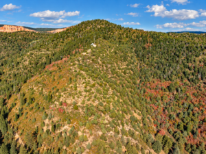 Rocky, forested hill with distant orange cliffs and a small building on the slope