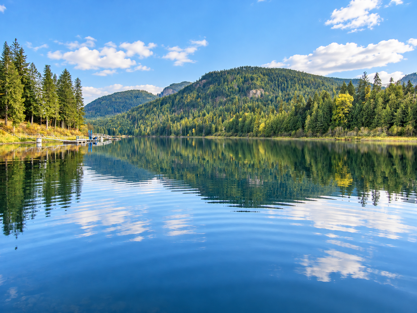 Calm Bull Lake water reflecting evergreen forests, mountains and clouds near Troy, Montana